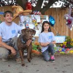 Kevin Cassidy and his daughter Alabama, 7, stand with their dog Remington by a memorial for their family dog Stolli, whom the community has honored with notes and treats after her death Aug. 31. Alabama said Stolli was a nice dog and she had no idea so many people loved her dog. She&rsquo;s been taking people&rsquo;s notes and placing them in plastic bags to preserve them all. (Matthew Nash/Olympic Peninsula News Group)
