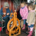 Alexia Fuller, 5, center, and Adeline Slezak, 3, both of Sequim, watch as Alison Sell, a member of the North Olympic Shuttle and Spindle Guild, spins wool into fiber at Lurkalee Gaare sheep farm near Agnew, one of seven farms and businesses taking part at the 20th annual Clallam County Farm Tour on Saturday. The event served as a celebration of agriculture and farmland. (Keith Thorpe/Peninsula Daily News)