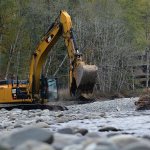 Crews work Tuesday to place large boulders around the base of each of the piers of the Elwha River bridge on U.S. Highway 101 to slow the rate of erosion. (Jesse Major/Peninsula Daily News)