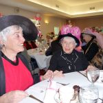 Patricia Morrison Coate/Olympic Peninsula News Group Thelma Bullock, left, is one of eight organizers of the Mad Hatters Tea Party. Seated next to her is 87-year-old Betty Newlon sporting her Betty&rsquo;s Boobs hat and the message of &ldquo;Fishing for a Cure.&rdquo;