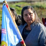 Frances Charles, Lower Elwha Klallam Tribe chairwoman, holds a flag for the Standing Rock Sioux Tribe as she listens to tribal members sing the Help Song in support of the Standing Rock Sioux at a gathering at the mouth of the Elwha River on Thursday. (Jesse Major/Peninsula Daily News)