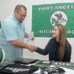 Keith Thorpe/Peninsula Daily News                                Port Angeles High School senior Kiana Robideau, seated, receives congratulations from athletic director Dwayne Johnson prior to Robideau signing a letter of intent on Wednesday to attend Evergreen State College on a volleyball scholarship.