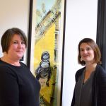 OlyCAP staff members Marki Lockhart, left, and Laura Calabria frame a painting given to the agency by artist and Peninsula Home Fund beneficiary Erica McClain. (Diane Urbani de la Paz/for Peninsula Daily News)