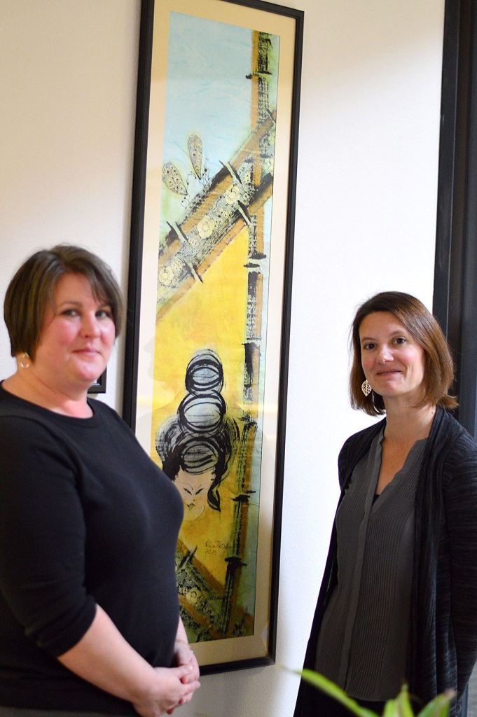 OlyCAP staff members Marki Lockhart, left, and Laura Calabria frame a painting given to the agency by artist and Peninsula Home Fund beneficiary Erica McClain. (Diane Urbani de la Paz/for Peninsula Daily News)