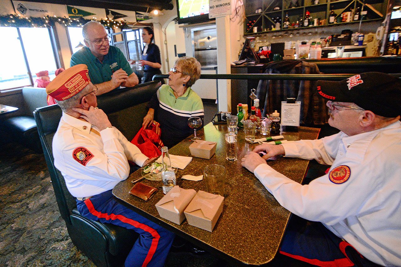 Marine Corps veterans Mark Schildknecht, front left, and Guy Iredale, right, chat with Smuggler&rsquo;s Landing owner Rick Mathis after the free meal he gave veterans last week. (Jesse Major/Peninsula Daily News)