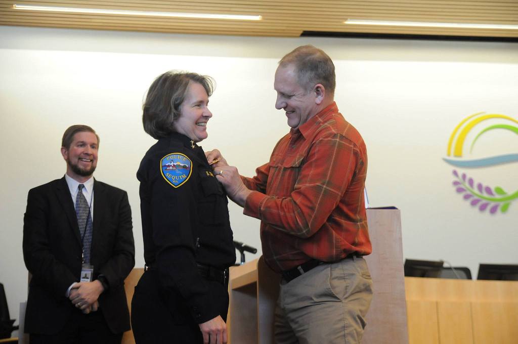 Pat Crain pins the Sequim police chief badge on his wife Sheri after she was sworn into office on December 16. Sequim City Manager Charlie Bush, left, chose her without an interview process following the retirement of Bill Dickinson earlier in December. Sequim Gazette photo by Michael Dashiell