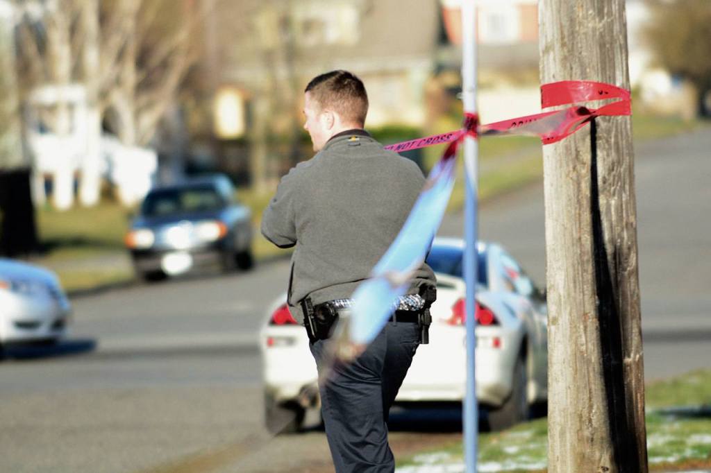 Detective Shane Martin of the Port Angeles Police Department puts police tape around 201 W. Ninth Street, where police say a man shot and killed his father. (Jesse Major / Peninsula Daily News)
