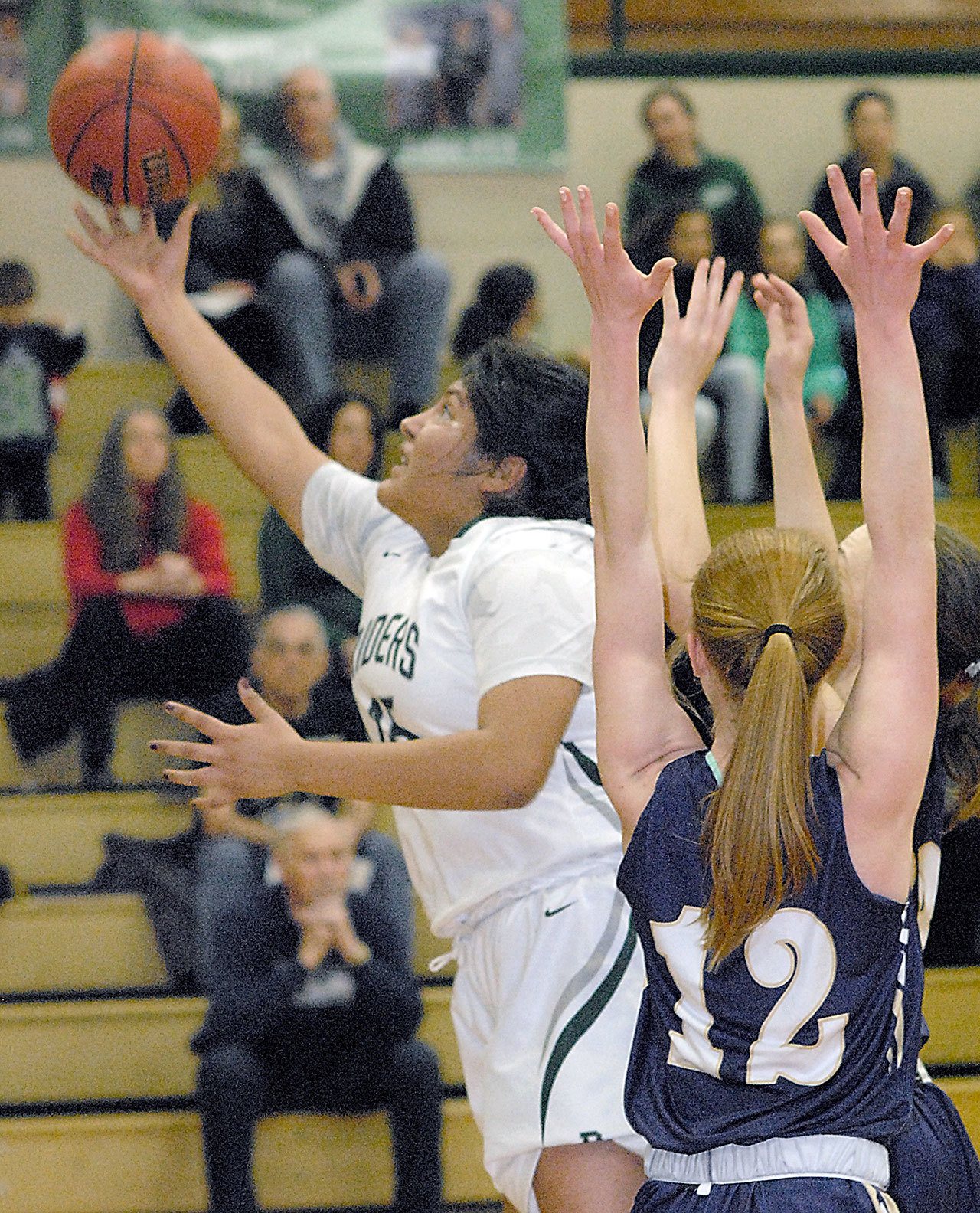 Keith Thorpe/Peninsula Daily News Port Angeles&rsquo; Nizhoni Wheeler, left, squeezes between the defense of North Kitsap&rsquo;s Ashley Vest, front right, and Raelee Moore for a layup attempt in the first quarter of play on Tuesday at Port Angeles High School.