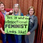 Robin Stemen, Susan Sherman and Annemarie Mende hold up one of the signs they&rsquo;re taking to the Womxn&rsquo;s March in Seattle on Saturday. (Cydney McFarland/Peninsula Daily News)