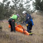 Maura Treaccar of Olympic Mountain Rescue, left, and Lee Oman of the Clallam County Fire District No. 3 rescue team adjust a folding carrier on a hillside at the former Clallam County landfill during Wednesday&rsquo;s training session in Port Angeles. (Keith Thorpe/Peninsula Daily News)