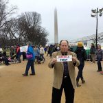 Joseph Lujan of Port Angeles stands with an &ldquo;America First&rdquo; sign during the Women&rsquo;s March on Washington last week after he attended President Donald J. Trump&rsquo;s inauguration Jan. 20.