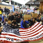 Demonstrators sit down in the concourse and hold a sign that reads &ldquo;We are America&rdquo; as more than 1,000 people gather at Seattle-Tacoma International Airport on Saturday to protest President Donald Trump&rsquo;s order that restricts immigration to the U.S. (Genna Martin/seattlepi.com via AP)