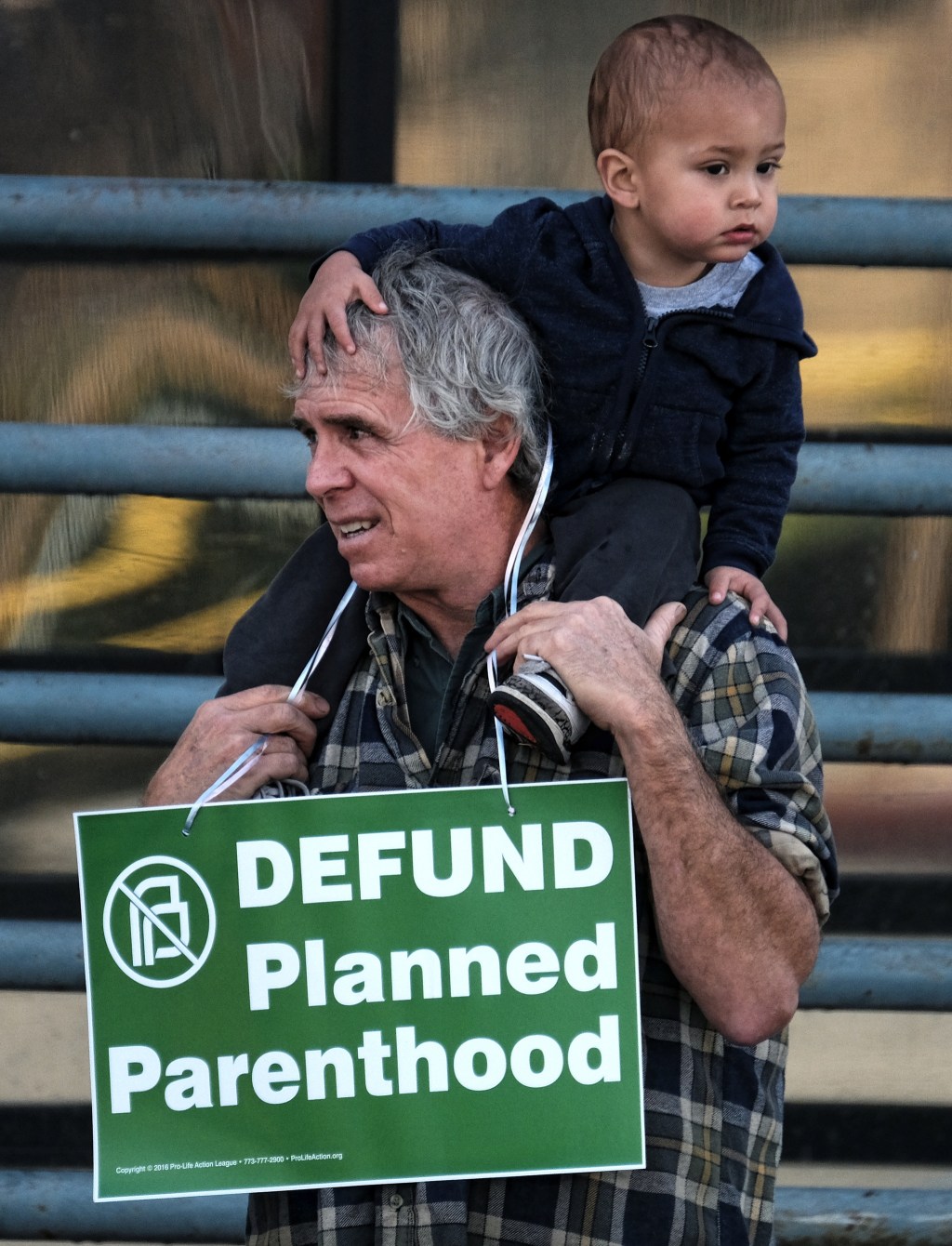 Ed Carver, holding his son, protests outside a Planned Parenthood health center in the Van Nuys section of Los Angeles on Saturday. Several dozen protesters gathered in California&rsquo;s San Fernando Valley demanding the organization be stripped of its federal funding. (Richard Vogel/The Associated Press)