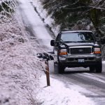 A vehicle travels on the snow-covered Dan Kelly Road west of Port Angeles on Sunday. (Jesse Major/Peninsula Daily News)