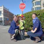 Jefferson County Farmers Market assistant manager Amy Costa Goetz and her son, Mikah, at left, wearing a farmers market hat; and market director Amanda Milholland stand on the corner of Lawrence and Tyler streets in Port Townsend, where the farmers market will kick off its 2017 season Saturday. (Cydney McFarland/Peninsula Daily News)