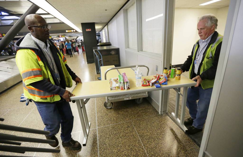 Port of Seattle workers Aaron Washington, left, and Tracy Jenkins carry a table and snacks into a room near where passengers arrive on international flights at Seattle-Tacoma International Airport on Tuesday. (Ted S. Warren/The Associated Press)
