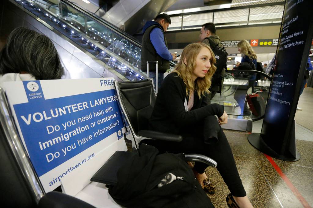 Asti Gallina, left, a volunteer law student from the University of Washington, sits at a station near where passengers arrive on international flights at Seattle-Tacoma International Airport on Tuesday. (Ted S. Warren/The Associated Press)                                Asti Gallina, left, a volunteer law student from the University of Washington, sits at a station near where passengers arrive on international flights at Seattle-Tacoma International Airport on Tuesday. (Ted S. Warren/The Associated Press)