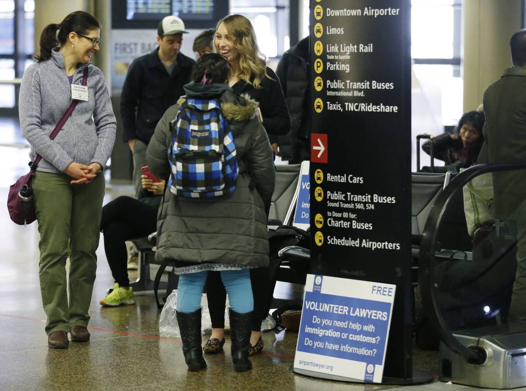 Asti Gallina, right, and Emily McDaniel, left, both volunteer law students, talk to a traveler as they staff a station near where passengers arrive on international flights at Seattle-Tacoma International Airport on Tuesday. (Ted S. Warren/The Associated Press)
