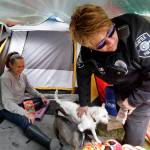 In this photo taken March 23, Seattle Police Officer Tawnia Pfaff, right, hands out biscuits to dogs belonging to Sheryl, a homeless woman who declined to give her last name, as part of a new team of outreach workers and officers that go out and connect homeless people to services in Seattle. Sheryl has lived in a tent in a greenbelt near Interstate Highway 90 for about six months. (Elaine Thompson/The Associated Press)