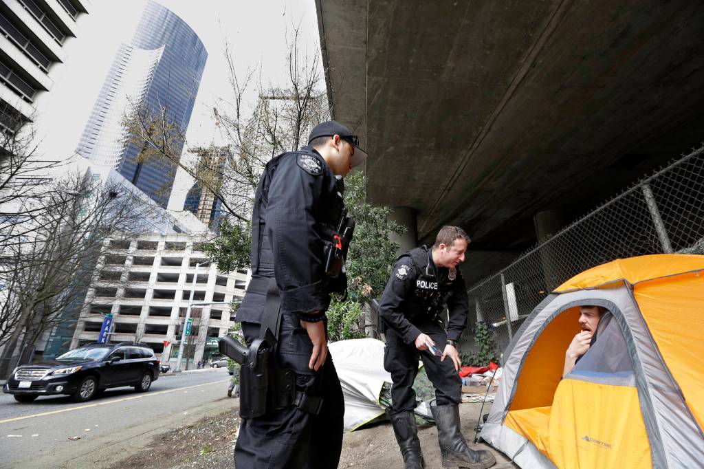 In this photo taken March 23, Seattle Police Officers Wes Phillips, left, and Tori Newborn talk with Corvin Dobschutz as part of a new team of outreach workers and officers that go out and connect homeless people to services, as the homeless man sits in his tent below a freeway and next to downtown Seattle. (Elaine Thompson/The Associated Press)