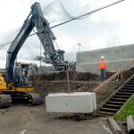 Port Angeles Lefties co-owner Jake Oppelt, right, watches as a loader operated by Jamey Watts of Lakeside Industries hoists a concrete retaining block into place behind a new home team dugout at Port Angeles Civic Field on Saturday. Lakeside contributed the use of its employees and equipment to help with modifications to the field to accommodate the start of West Coast League baseball on June 1. (Keith Thorpe/Peninsula Daily News)