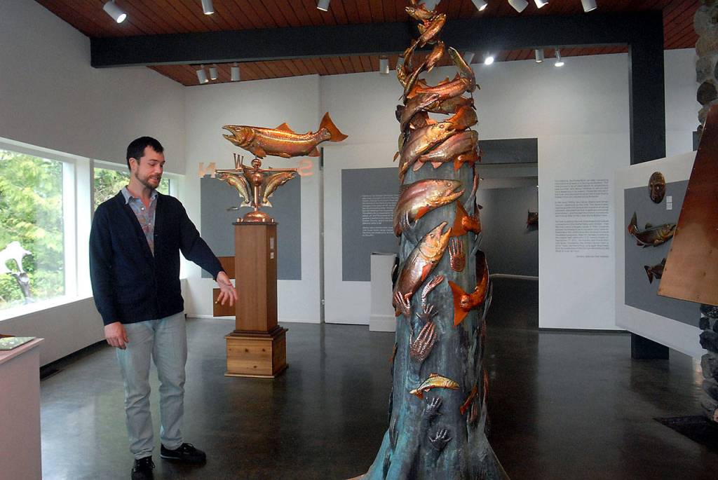 Exhibit curator Randy Powell discusses the sculpture &ldquo;Our Elwha&rdquo; by copper artist Clark Mundy as another Mundy sculpture, &ldquo;Four Winds,&rdquo; stands in the background in the main room of the Port Angeles Fine Arts Center. (Keith Thorpe/Peninsula Daily News)