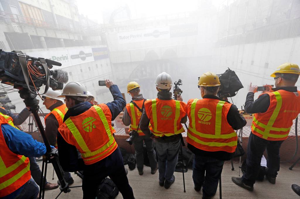 Media members look on as dust fills a pit below while a massive tunneling machine nears breaking through a 5-foot concrete wall into the disassembly area for the state Highway 99 route Tuesday under Seattle. (Elaine Thompson/The Associated Press)