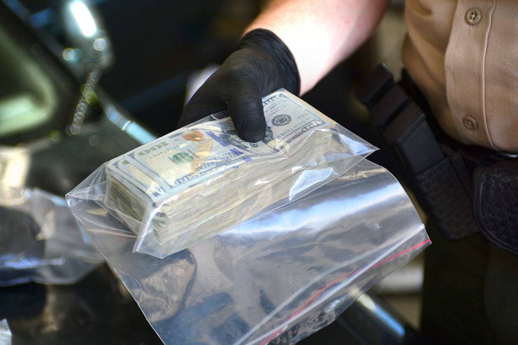 A Clallam County Sheriff&rsquo;s deputy holds a wad of cash, made up mostly of $20s, discovered during a vehicle search Sunday. (Jesse Major/Peninsula Daily News)