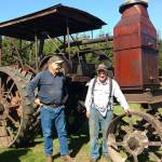 John Spoelstra and Rene Davis share a laugh in the sun near one of three classic Rumely farm tractors owned by Spoelstra&rsquo;s uncle, Ted Spoelstra. (Zorina Barker/for Peninsula Daily News)