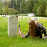 Oracle Holms of Port Hadlock places flags at the gravestones of veterans in the cemetery at Fort Worden on Monday. (Cydney McFarland/Peninsula Daily News)