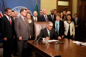 Gov. Jay Inslee, seated, prepares to sign a bill Tuesday in Olympia that seeks to bring Washington state into compliance with the federal REAL ID Act. (Rachel La Corte/The Associated Press)
