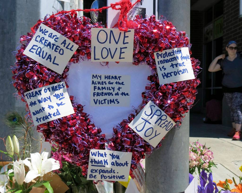 A heart-shaped wreath covered with positive messages hangs on a traffic light pole at a memorial for two bystanders who were stabbed to death Friday while trying to stop a man who was yelling anti-Muslim slurs and acting aggressively toward two young women, including one wearing a Muslim head covering, on a light-trail train in Portland, Ore. A memorial grew all day Saturday outside the transit center in Portland, as people stopped with flowers, candles, signs and painted rocks. (Gillian Flaccus/The Associated Press)