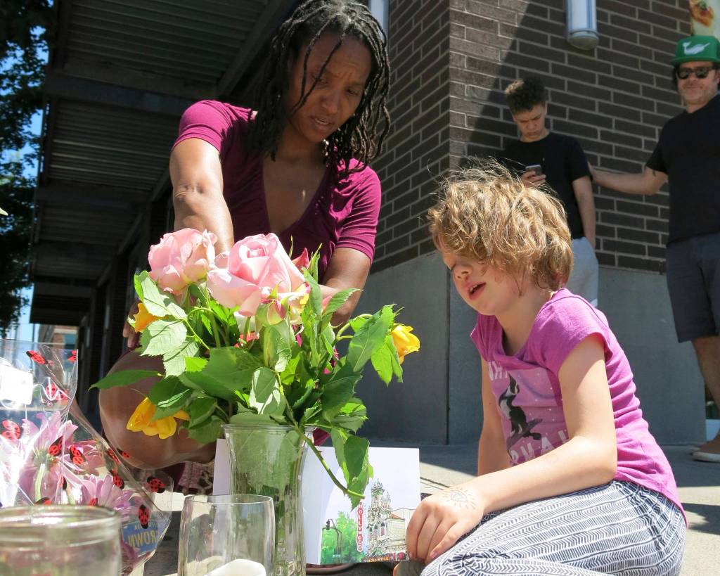 Angel Sauls, left, helps her stepdaughter, Coco Douglas, arrange a sign and some painted rocks she made for a memorial in Portland, Ore., on Saturday for two bystanders who were stabbed to death Friday while trying to stop a man who was yelling anti-Muslim slurs and acting aggressively toward two young women. (Gillian Flaccus/The Associated Press)