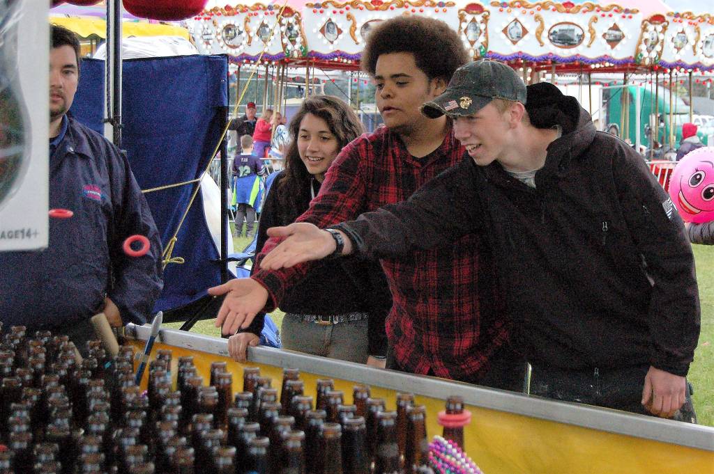 Sequim friends, from left, Anna Laurie, Trevor Jones and Payton Gagnon, all 18, enjoy a round of ring toss at the Sequim Irrigation Festival&rsquo;s carnival Saturday. It was Gagnon&rsquo;s first time at the carnival, he said, and they all had fun. (Matthew Nash/Olympic Peninsula News Group)