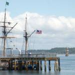 A passerby checks out the Hawaiian Chieftain, a tall ship docked at the Northwest Maritime Center, while another tall ship lowers its sails in the background, heading toward Marrowstone Island. (Cydney McFarland/Peninsula Daily News)