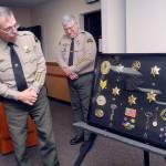 Clallam County Sheriff Bill Benedict, left, looks over a shadowbox of badges, patches and other memoribilia from the career of retiring county Jail Superintendent Ron Sukert, center, during a presentation honoring Sukert on Tuesday at the Clallam County Courthouse. (Keith Thorpe/Peninsula Daily News)