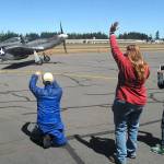Ricki McLaughlin of Port Angeles, center, waves at the arrival of a vintage TF-51D Mustang as Kelly Thomas of Sequim, left, and Jenna McGoff, 13, of Port Angeles take photos Wednesday. (Keith Thorpe/Peninsula Daily News)