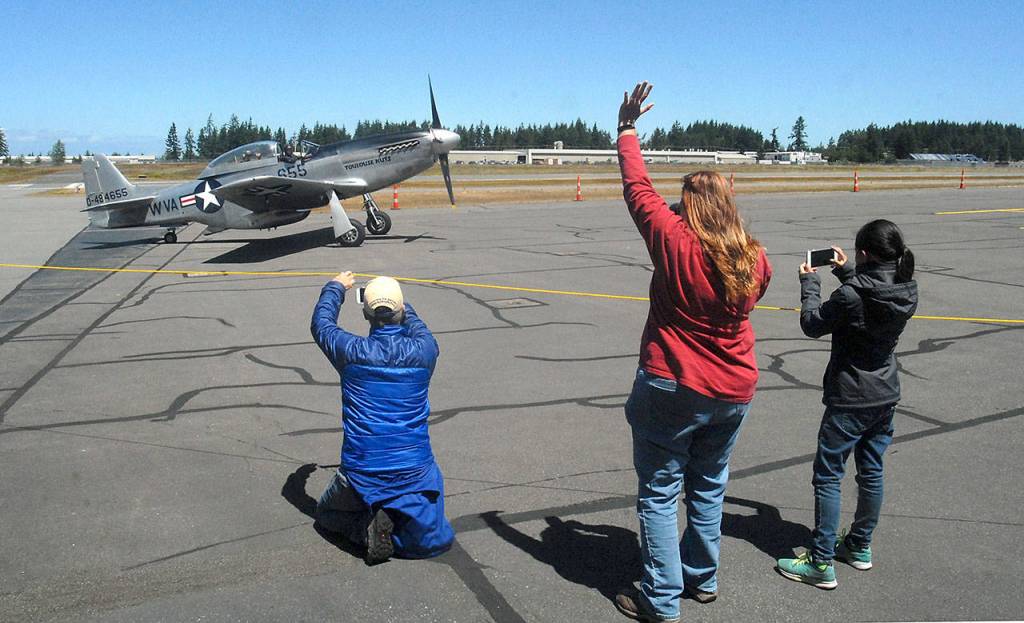 Ricki McLaughlin of Port Angeles, center, waves at the arrival of a vintage TF-51D Mustang as Kelly Thomas of Sequim, left, and Jenna McGoff, 13, of Port Angeles take photos Wednesday. (Keith Thorpe/Peninsula Daily News)