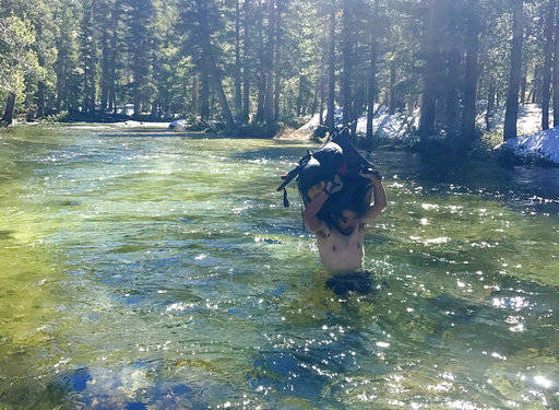 In this June 15 photo, Jake Gustafson crosses wading chest-deep in still waters with his backpack over his head at Evolution Creek along the Pacific Crest Trail near Kings Canyon National Park, Calif. (Wesley Tils via AP)