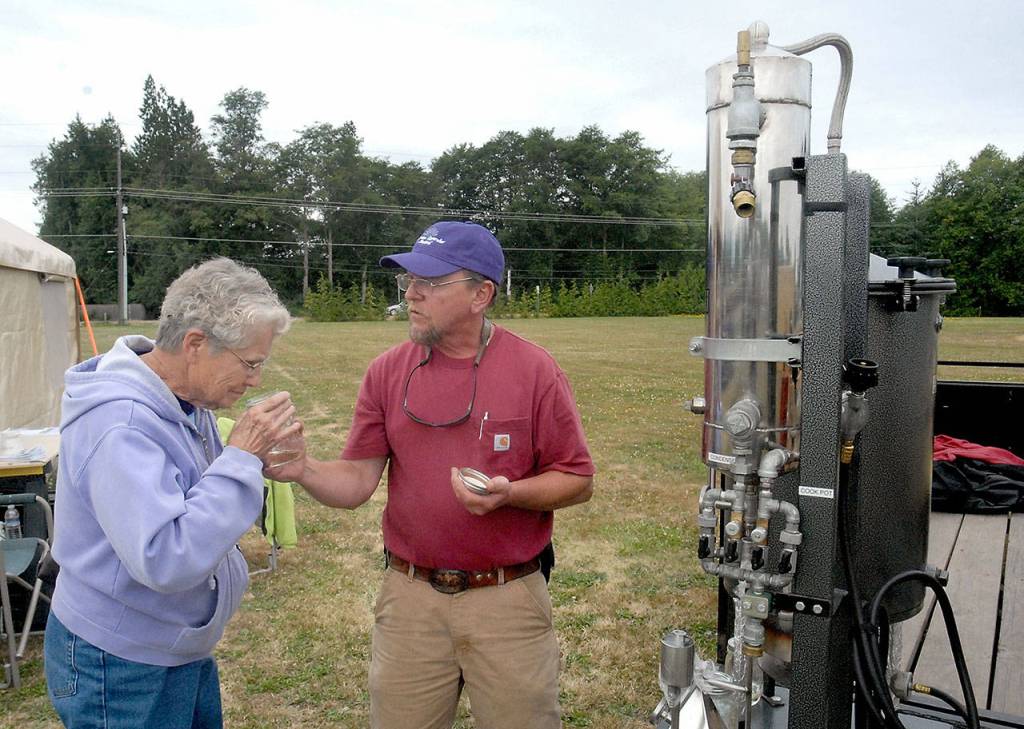 Doris Causey of Sequim, left, sniffs a sample of concentrated lavender distilled by Richard Pinder, owner of Earth Muffin Lavender, on Friday, the first day of Sequim Lavender Weekend. (Keith Thorpe/Peninsula Daily News)