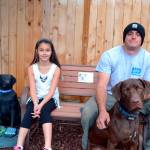 Alabama and her dad, Kevin Cassidy, sit last October with their dog Remington on a bench that memorializes family dog Stolli, who died Aug. 31, 2016. The statue to the left was reported stolen Thursday and recovered broken later in the day. Community members look to fund a replacement for the Cassidy family. (Matthew Nash/Olympic Peninsula News Group)