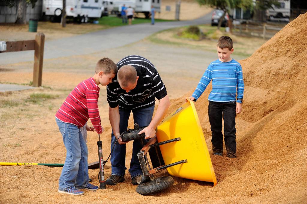 Jeff Bender, with help from his sons Daniel, 9, left, and Grant, 8, right, tries to fix a flat tire on a wheelbarrow outside the swine barn at the Clallam County Fair. Daniel belongs to Pure Country 4-H and will show pigs, rabbits and goats throughout the fair. (Matthew Nash/Olympic Peninsula News Group)
