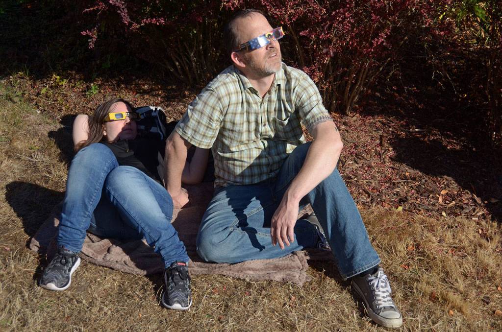 Lauren Davis and Charlie Arthur watch Monday&rsquo;s eclipse through protective glasses in the grass in front of the Port Townsend Library along with over 200 other people. (Cydney McFarland/Peninsula Daily News) ​