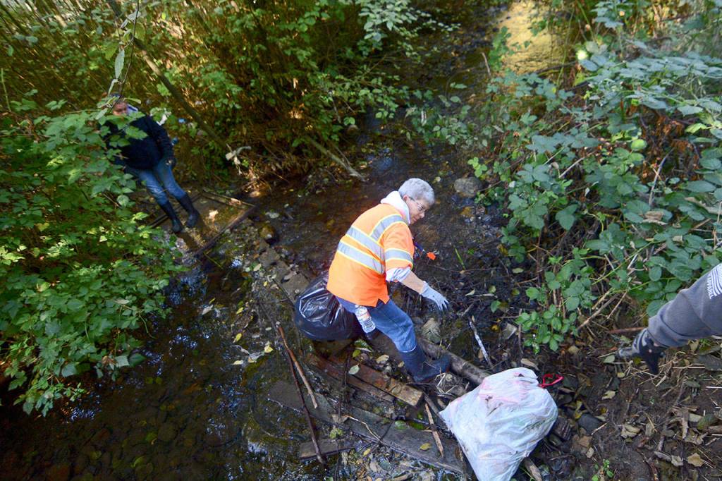 Patty Pastore stands on a makeshift bridge spanning Tumwater Creek as crews remove trash from an abandoned camp Oct. 15. (Jesse Major/Peninsula Daily News)