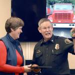 Sam Phillips, chief of Clallam County Fire District No. 2, right, holds up the keys to a refurbished brush truck used for fighting wildland fires after receiving them from Julie Knobel, assistant regional manager for the state Department of Natural Resources, during a ceremony in Port Angeles. The truck, shown on the screen in the background, was acquired by the department through a DNR surplus program that allocates used firefighting equipment to local agencies around the state. (Keith Thorpe/Peninsula Daily News)