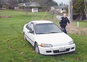 Port Angeles Police Officer David Drombowski examines a car that was driven through backyards and then abandoned behind 1723 Lambert Lane after a short chase in Port Angeles. (Keith Thorpe/Peninsula Daily News)