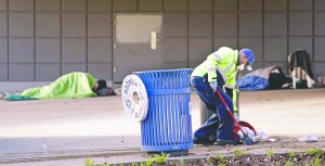 A contract worker cleans up trash Tuesday as men continue to sleep behind him under a Seattle overpass near where police arrested three teenage boys.  The Associated Press ()