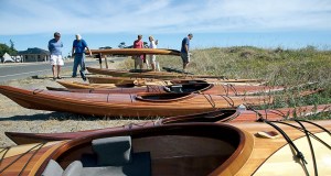 Kayak enthusiasts examine a custom-built wooden kayak amid many lined up during the 17th annual West Coast Wooden Kayak Rendezvous under sunny skies at Fort Worden State Park on Saturday. The gathering continues today. Steve Mullensky/for Peninsula Daily News