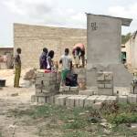 Matgid, a carpenter, stands to the left as, from left, an unidentified worker, Justin Adjogble, Kolawole Dokou and Jordan Amouzou, the master bricklayer, work on a Dignity Toilet.