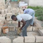Two unidentified bricklayer apprentices work on a toilet.